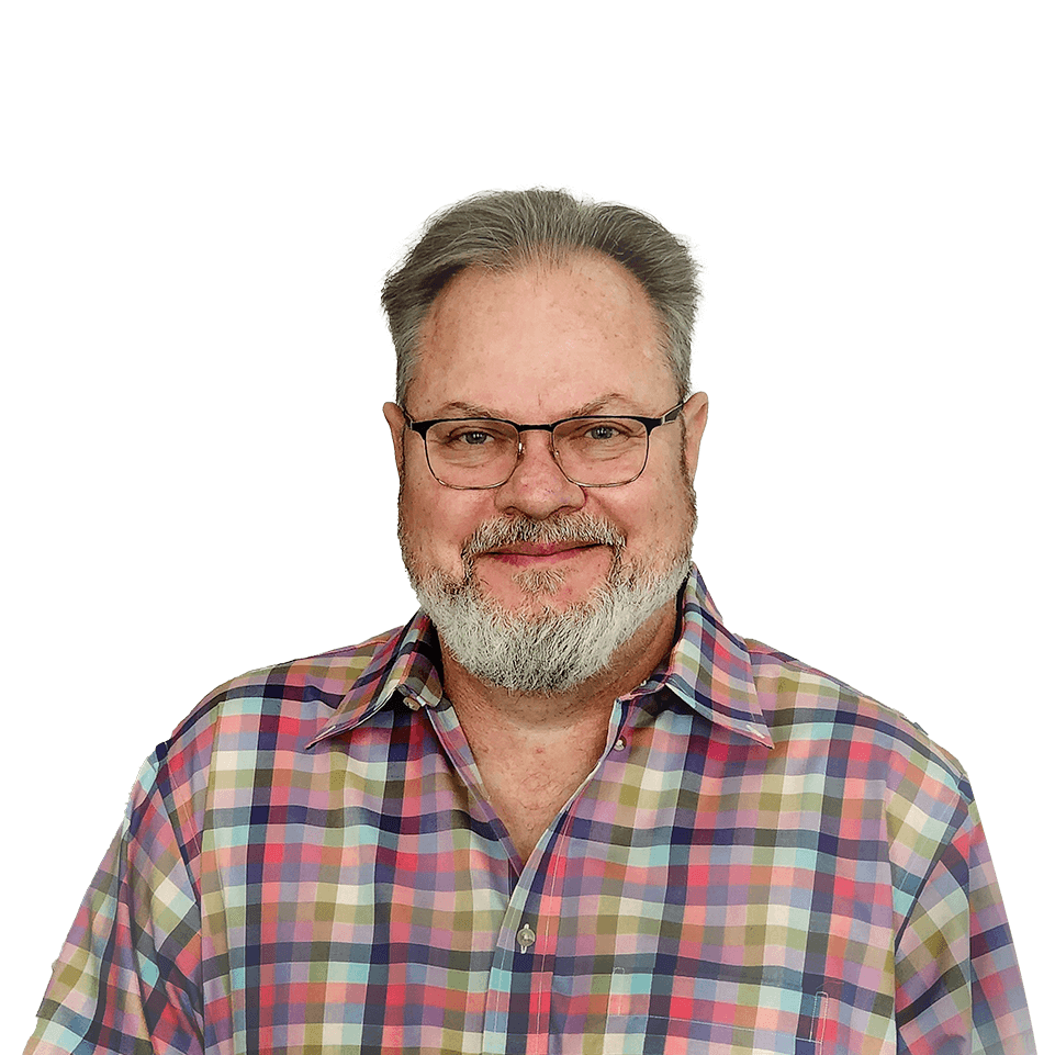 Jim smiling in a colorful checked shirt with a shady tree-lined patio with tables and chairs in the background