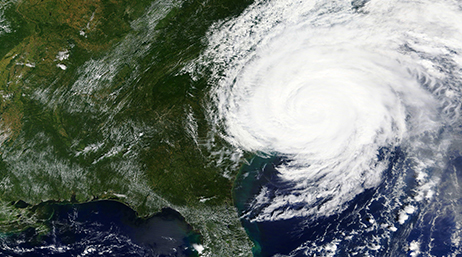 A satellite image of a hurricane swirling over a deep green landmass and dark blue ocean