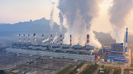 A large refinery plant with many smokestacks emitting large water vapor clouds 