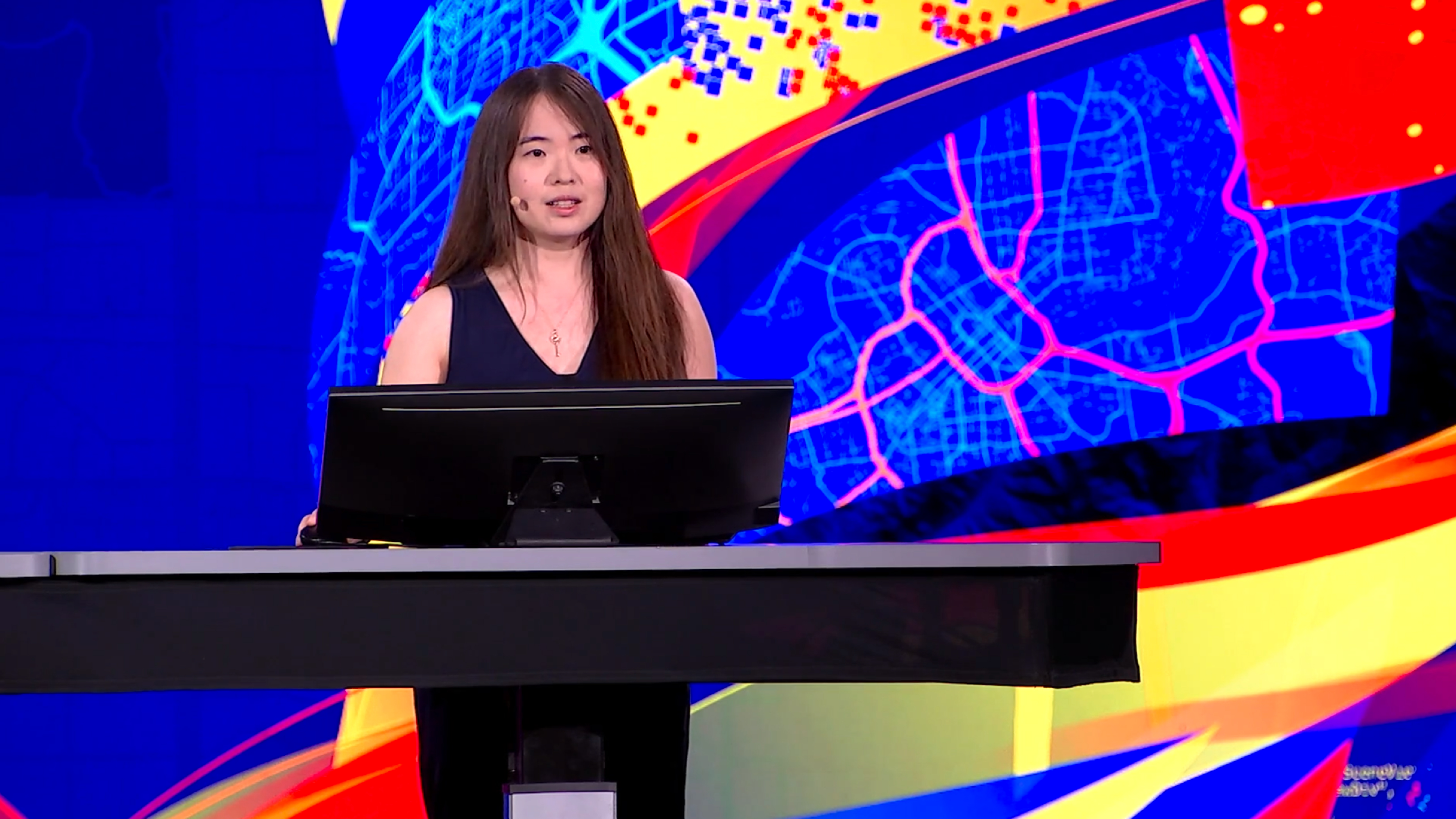A young woman in a blue dress standing behind a podium with a city map being projected behind her