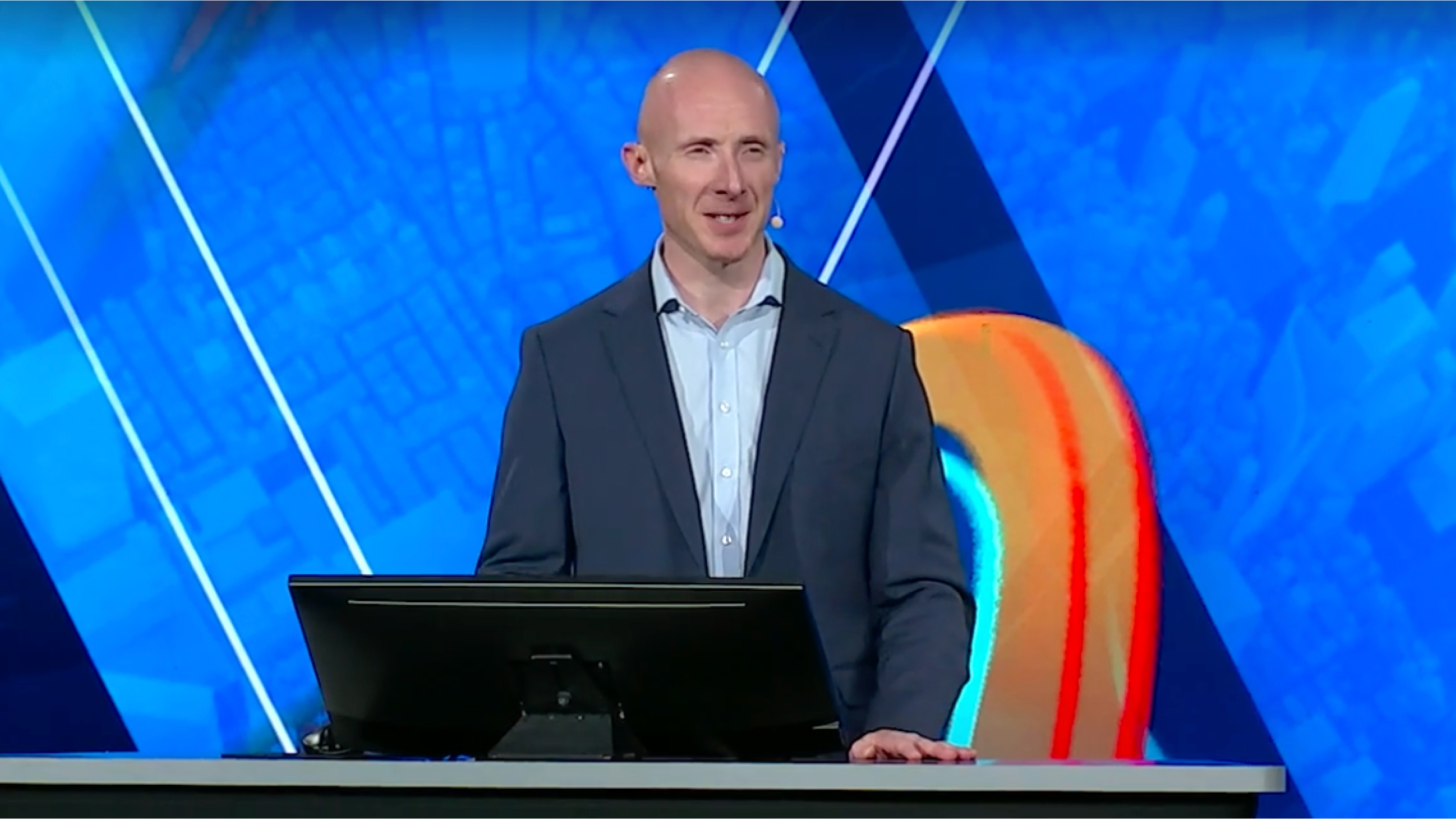 A man in a suit standing behind a podium and speaking to the camera