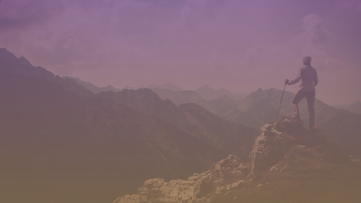 A hiker looking at a mountain range from the summit of another peak 