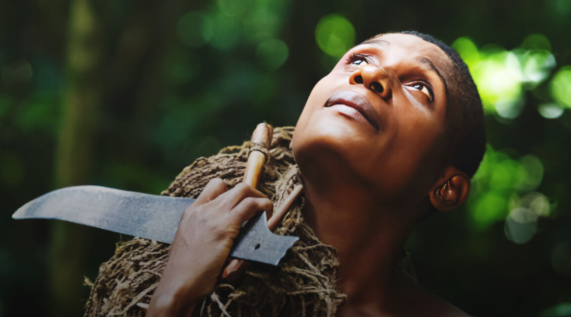 An indigenous person looking upward while walking through a forest