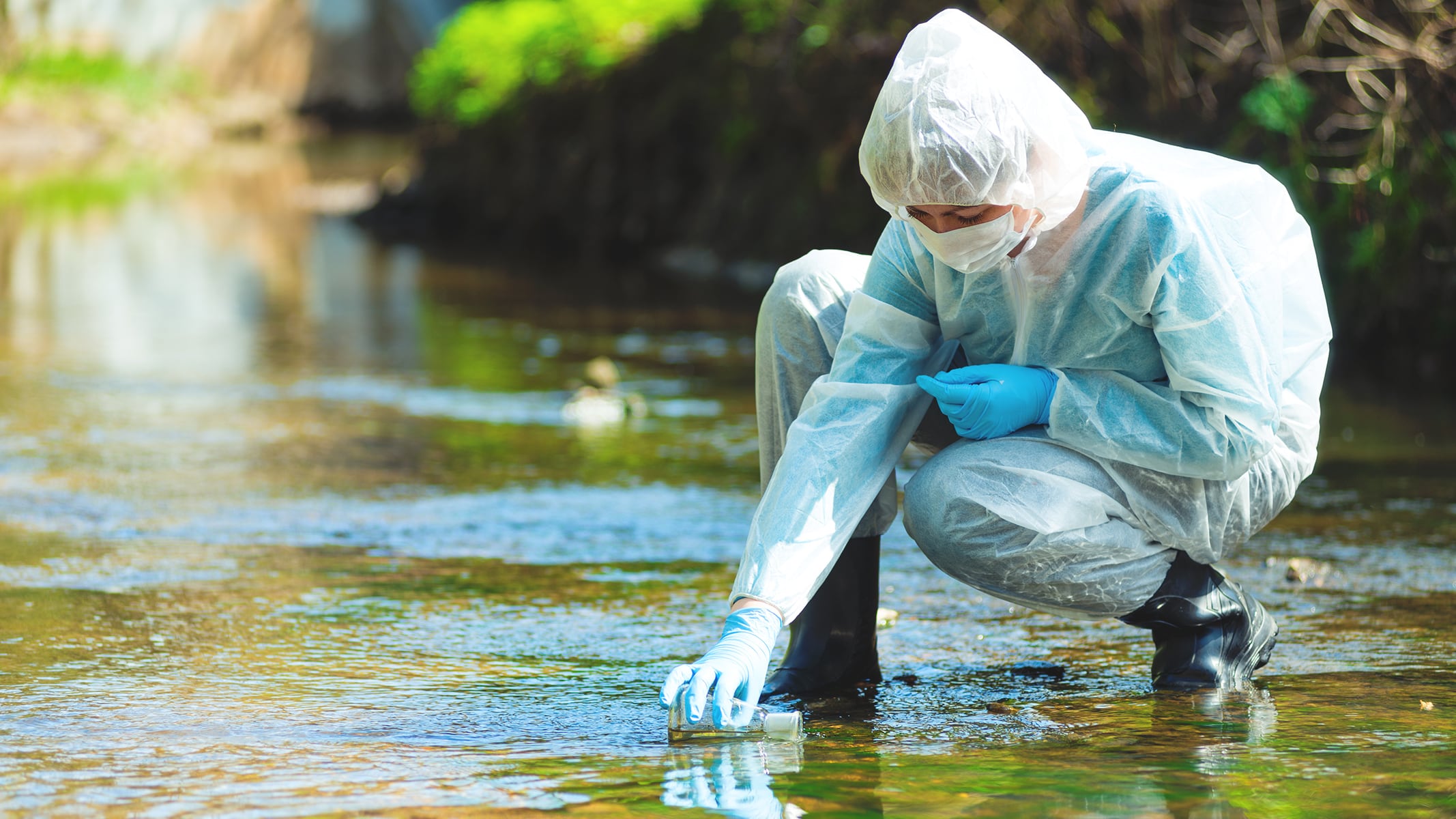 A technician in white coveralls testing water in a stream