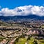 Aerial view of suburbs with houses in green foothills, looking towards snow-capped, clouded mountains