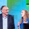 Three smiling students in blue polo shirts onstage at a conference with Jack Dangermond and Dawn Wright in front of a colorful abstract background