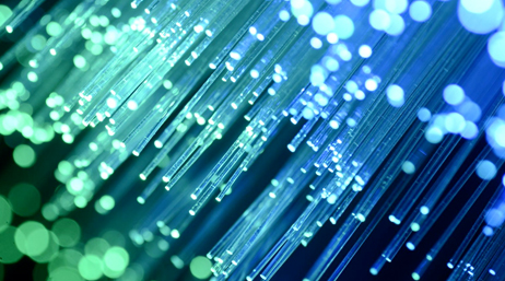 An extreme closeup photo of the ends of a cluster of fiber optic cables lit and glowing in shades of blue and green