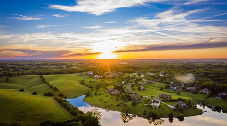 Rolling green hills dotted with homes as the sun sets in the distance 