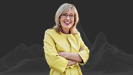 A smiling person wearing glasses and a yellow dress with their arms crossed overlaid on a wireframe of a mountain range