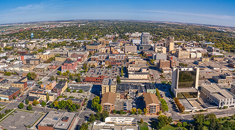 Aerial image of a sprawling North Dakota city with low buildings in pale brown dotted with trees under a clear blue sky