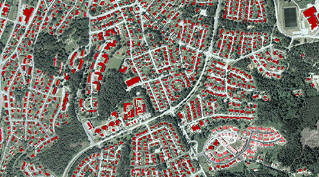 A developed area with structures highlighted in red surrounded by greenery 