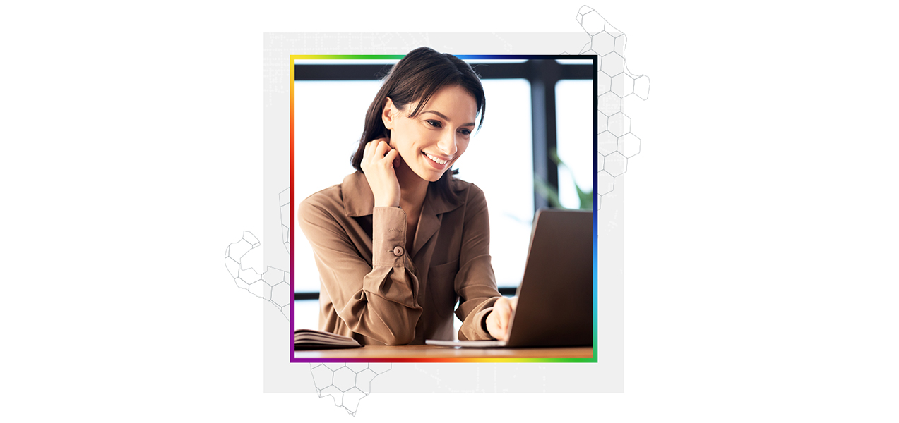 A smiling person in a pale brown collared shirt using a laptop in a modern sunlit office